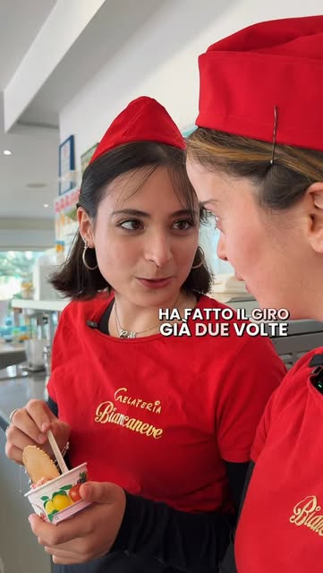 Coppetta di gelato con biscotto, tenuta in mano davanti alla vetrina refrigerata