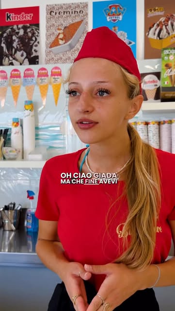 Gelataia dietro il bancone con le vaschette di gusti in esposizione